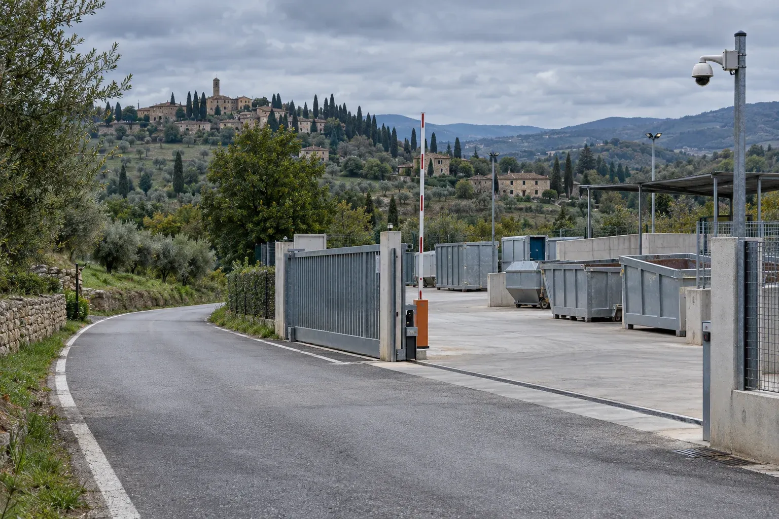 Ingresso di un centro di raccolta con cancello, sbarra e telecamera su palo, cassoni sul piazzale